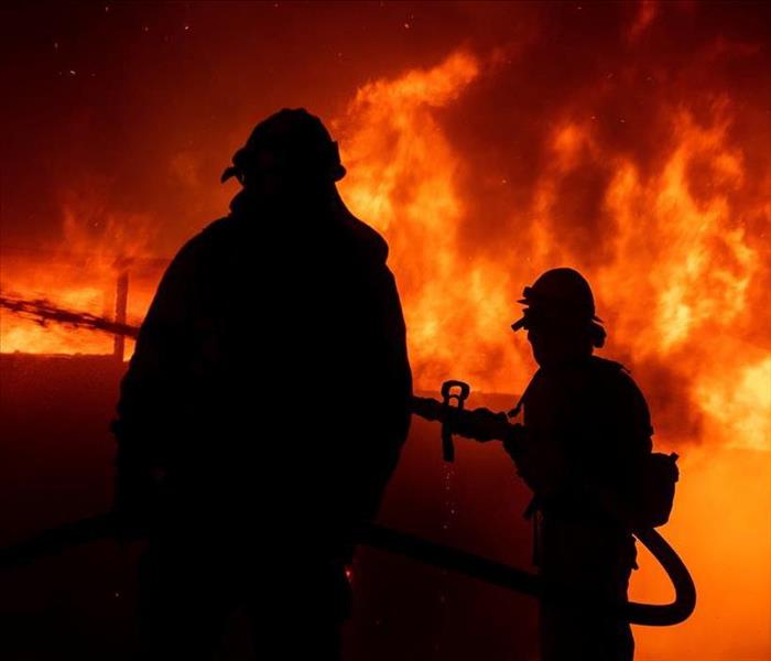 Two firefighters standing in front of a raging fire.