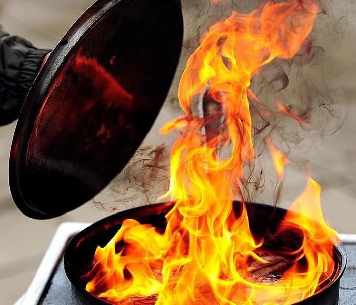 fire in a pot with a hand attempting to cover it with a pot lid